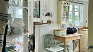 A cozy kitchen with a wooden table, a chair, a bookshelf, and a window with a view. - Two houses with a view of the fjord (Nibe)