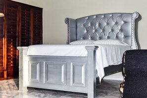 Una cama con cabecera capitonada, un armario de madera y una silla.