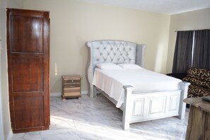 Een slaapkamer met een bed, een houten garderobe, een nachtkastje en een gestreept sofa.