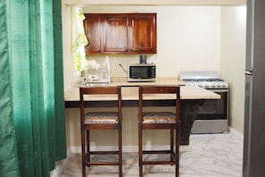 Una cocina con armarios de madera, microondas, estufa y dos sillas.