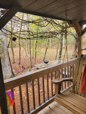 A wooden deck with a hanging chain, a barbecue grill, and a view of a forest with autumn leaves.