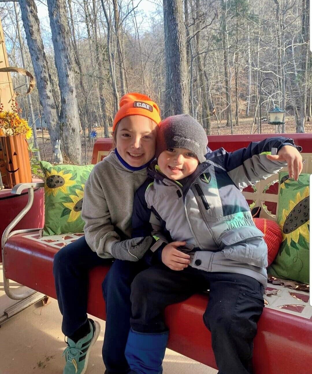 Dos niños sentados en un banco rojo, con un bosque de fondo.