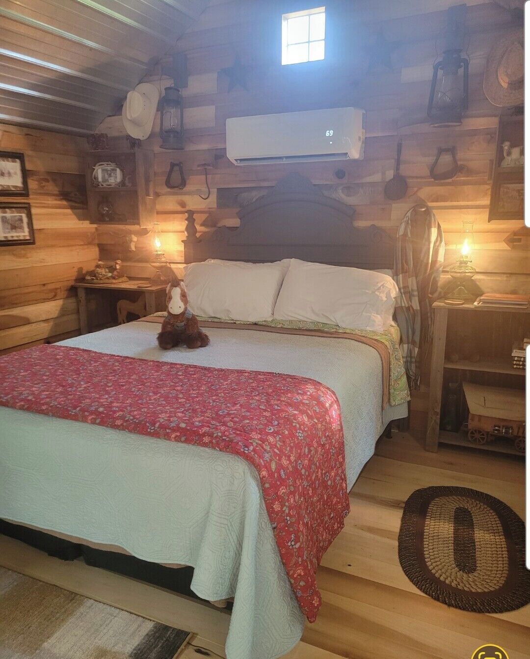 A wooden cabin-style bedroom with a bed, a nightstand, a lamp, a hanging lantern, and a small window.