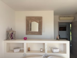 Una habitación con una consola blanca, un espejo, una lámpara pequeña y un aire acondicionado de pared.