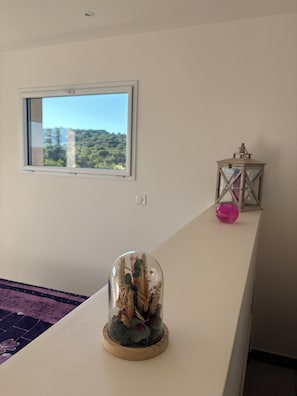 Una habitación con ventana, una cúpula de vidrio decorativa sobre un soporte de madera y un pequeño farol sobre una mesa.
