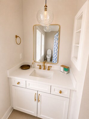 Een badkamer met een wit wastafelmeubel, gouden details en een spiegel met een gouden lijst.
