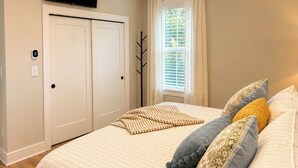 A bedroom with a bed, pillows, a ceiling fan, a TV, a window with curtains, and a door. - Beautiful Brand New Build 3-bedroom house in peaceful Rolesville 2 king bed (Rolesville)