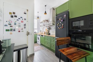 A kitchen with green cabinets, a Bosch refrigerator, a microwave, and a wooden chair. - Apartment T3 Premium -Paris- Parc des Princes 12 min walk (Boulogne-Billancourt)