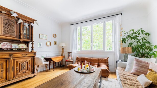 Una habitación con una mesa de comedor de madera, un sofá, una ventana con cortinas y una planta.