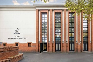 A brick building with large windows and a sign reading 'VILLE DE PARIS STADE PIERRE DE COUBERTIN'. - Apartment T3 Premium -Paris- Parc des Princes 12 min walk (Boulogne-Billancourt)