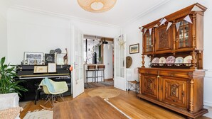 Una habitación con un piano, un aparador de madera, un rincón de comedor y una planta grande.