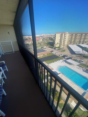 En balkon med udsigt over en swimmingpool, parkeringsplads og omkringliggende bygninger.