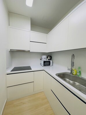 A small kitchen with white cabinets, a microwave, a sink, and a black countertop. - Nice Luxury Apartments The Sun Avenue (Ho Chi Minh City)