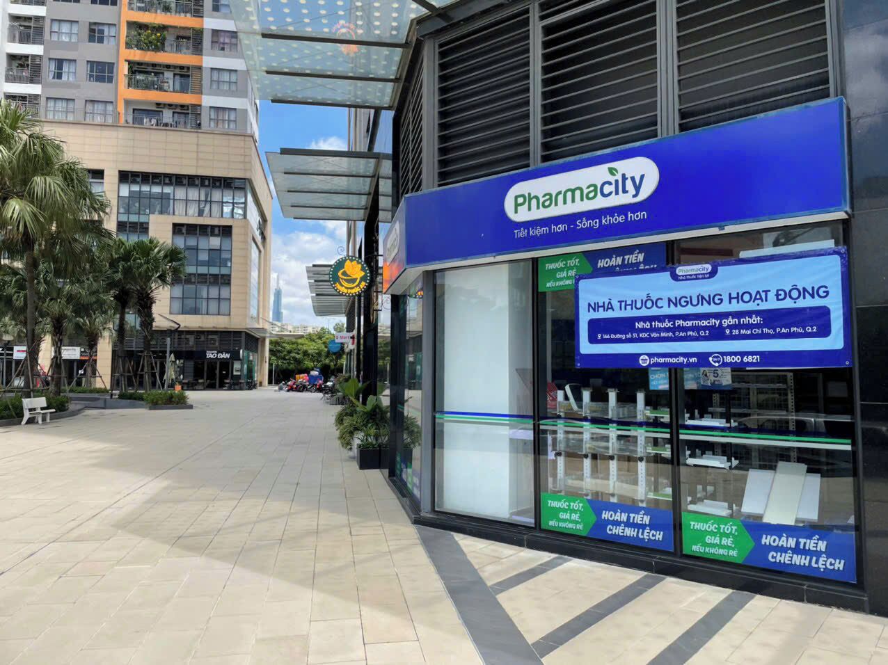 Une pharmacie avec une enseigne bleue, située dans une zone commerciale où se trouvent d’autres commerces.