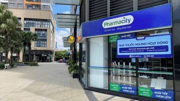 Une pharmacie avec une enseigne bleue, située dans une zone commerciale où se trouvent d’autres commerces.