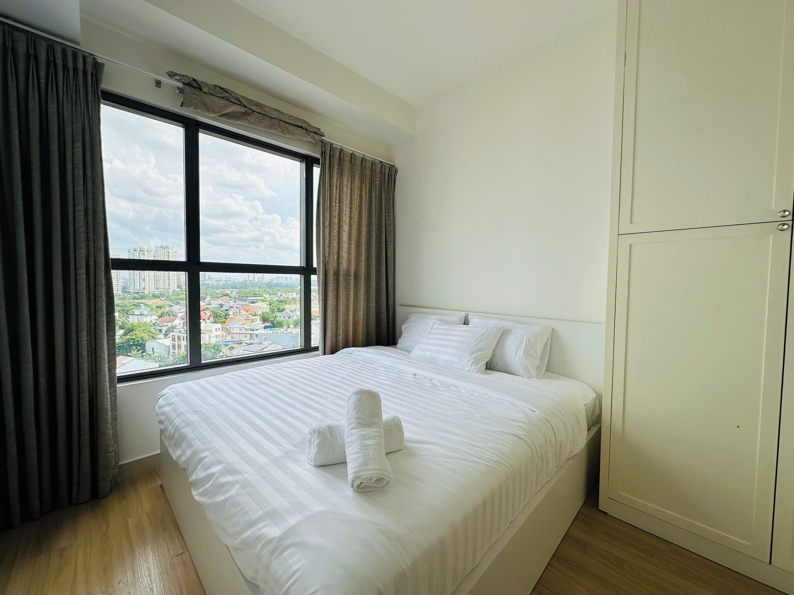 A hotel room with a large window, a bed with white linens, and a wardrobe.