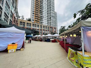 An outdoor market with tents and stalls, a woman with a child, and a tall building in the background. - Nice Luxury Apartments The Sun Avenue (Ho Chi Minh City)