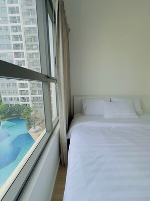 Una habitación de hotel con cama, ventana con cortinas y vistas a un edificio y una piscina.