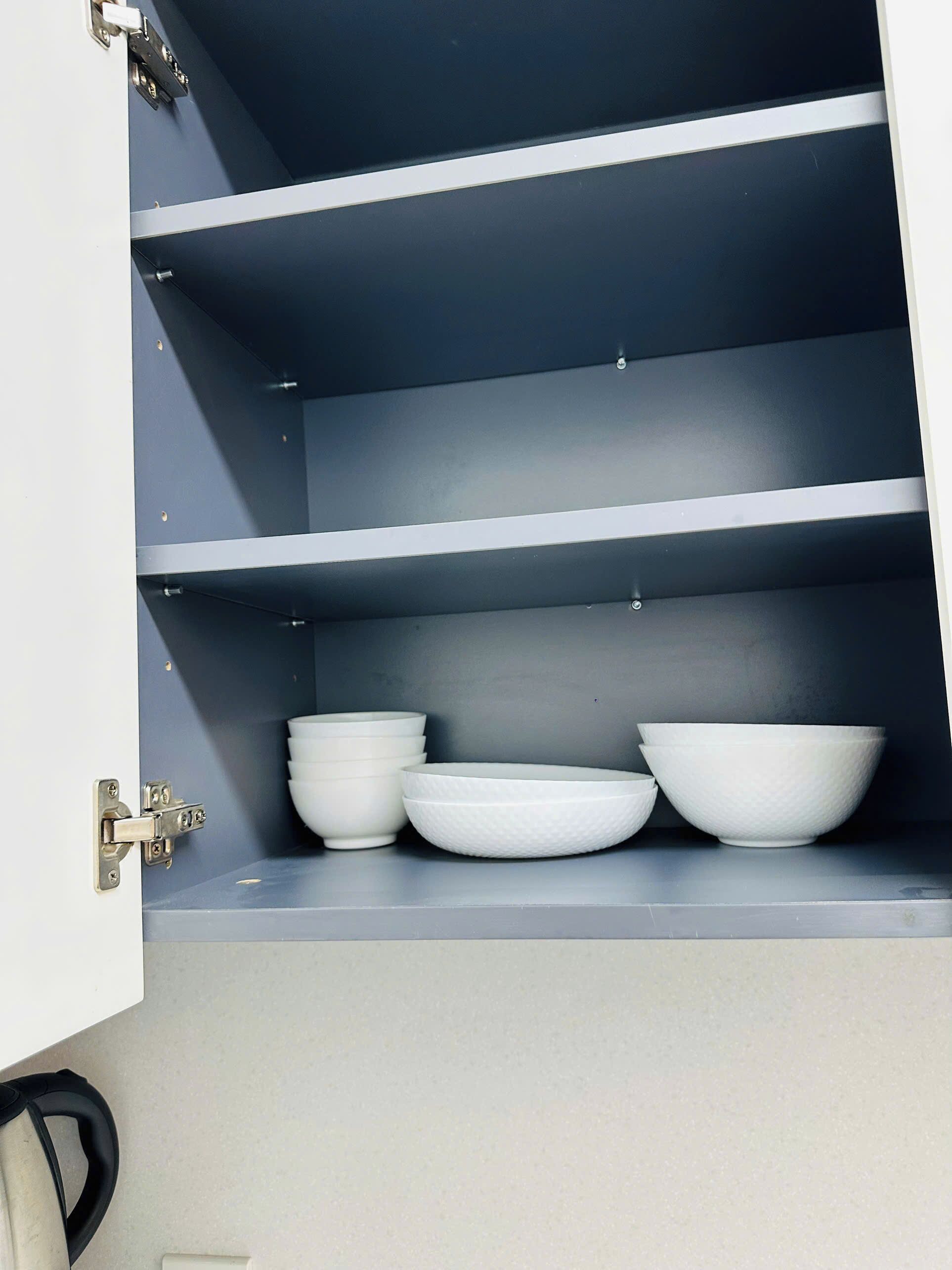 A kitchen cabinet with three white bowls on the middle shelf.