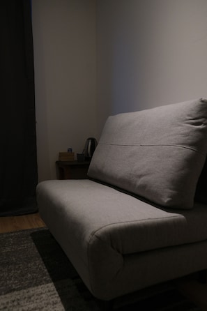 Un sofà gris en una habitació amb poca llum, amb un tamboret petit i una caixa al fons.