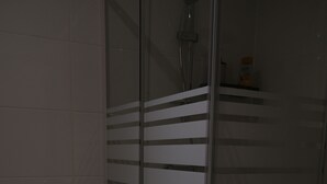 Un baño con cabina de ducha de vidrio, inodoro y un pequeño estante de madera con un objeto rojo.
