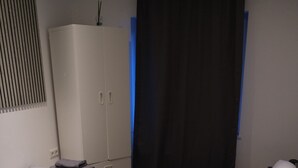Un dormitorio con cama, una silla, un armario, una mesita de noche y una ventana con cortina.