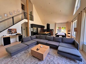 A spacious living area with a sectional sofa, a wooden coffee table, a kitchen with modern appliances, and a staircase.