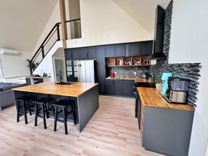 A modern kitchen with a central island, dark cabinetry, and a staircase leading to an upper level.