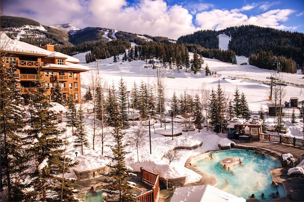 Een resort met een zwembadgedeelte, omringd door besneeuwde vlaktes en dennenbomen.