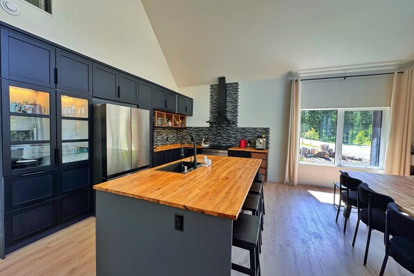A modern kitchen with a central island, dark cabinetry, and a stone fireplace. - Quiet detached home steps from all the action! (Panorama)