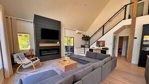 Una sala de estar moderna con un sofá modular, un televisor de pantalla plana, una chimenea y una escalera que conduce a un nivel superior.