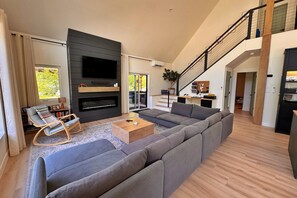 Ein modernes Wohnzimmer mit einer Eckcouch, einem Flachbildfernseher, einem Kamin und einer Treppe zu einer oberen Ebene.
