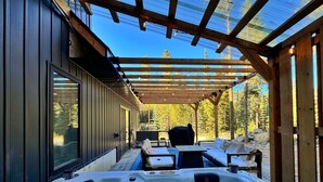 Un jacuzzi en un espacio exterior cubierto con una pérgola de madera, un área de descanso y vistas a árboles.