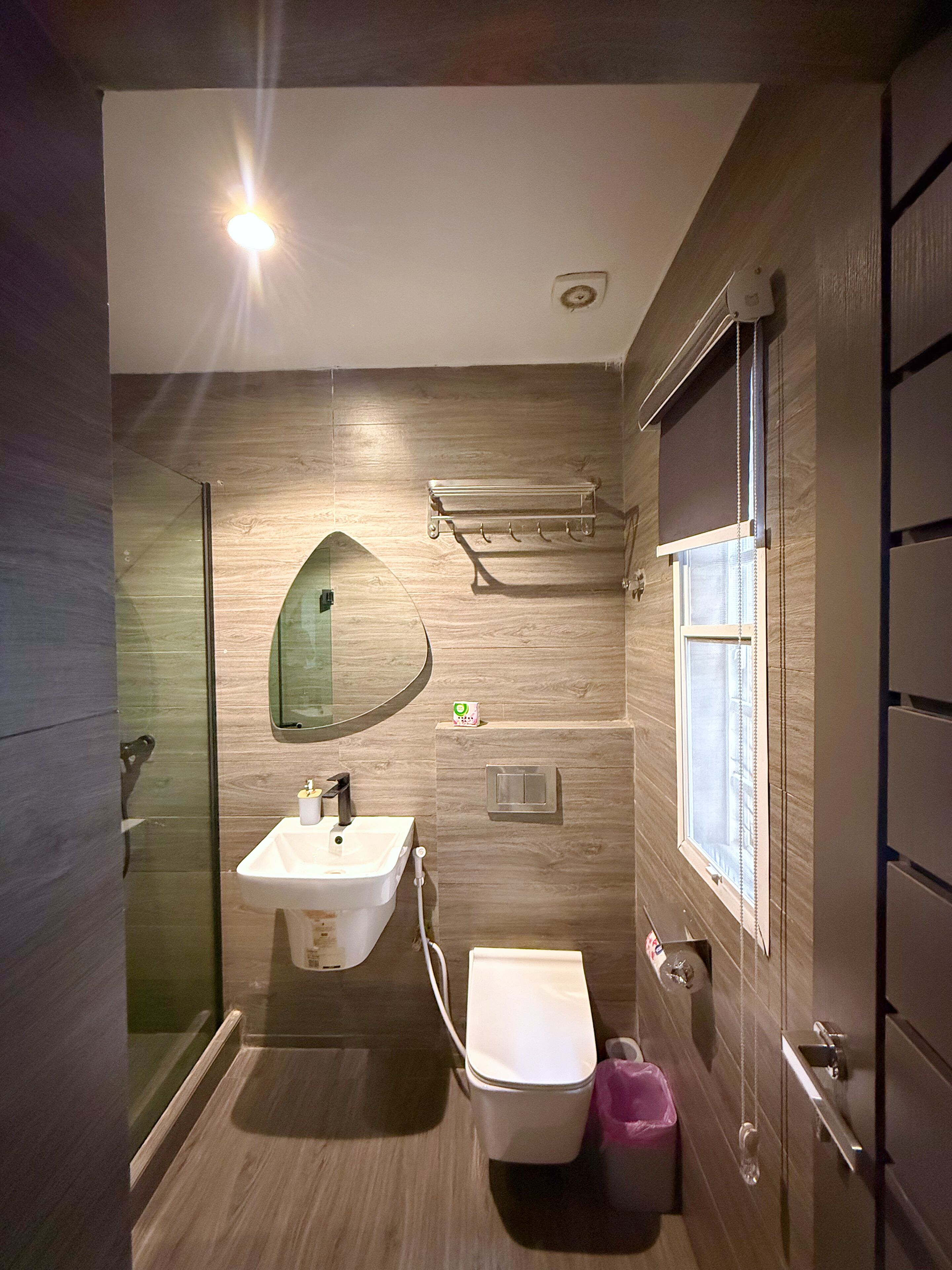 Un bagno moderno con cabina doccia in vetro, lavabo bianco, water e finestra con persiane.