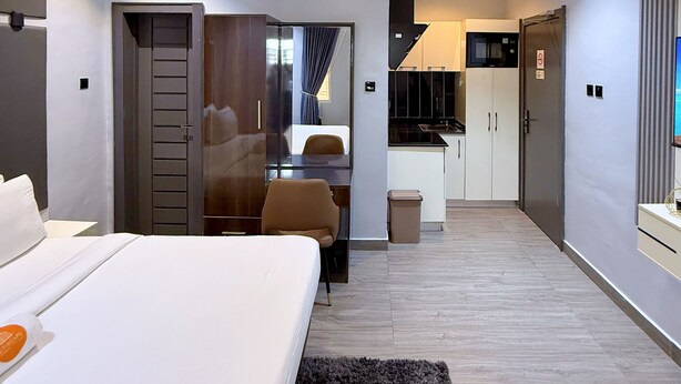 A modern hotel room with a bed, a desk, a chair, a small kitchen area, and a bathroom. - Citiscape Apartment (Ikeja)
