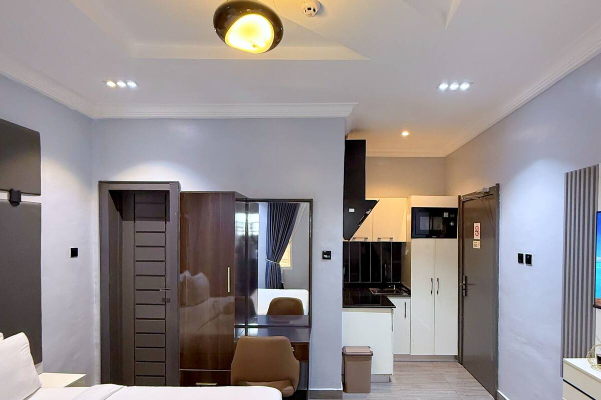 Habitación de hotel moderna con cama, escritorio, silla, kitchenette y baño.