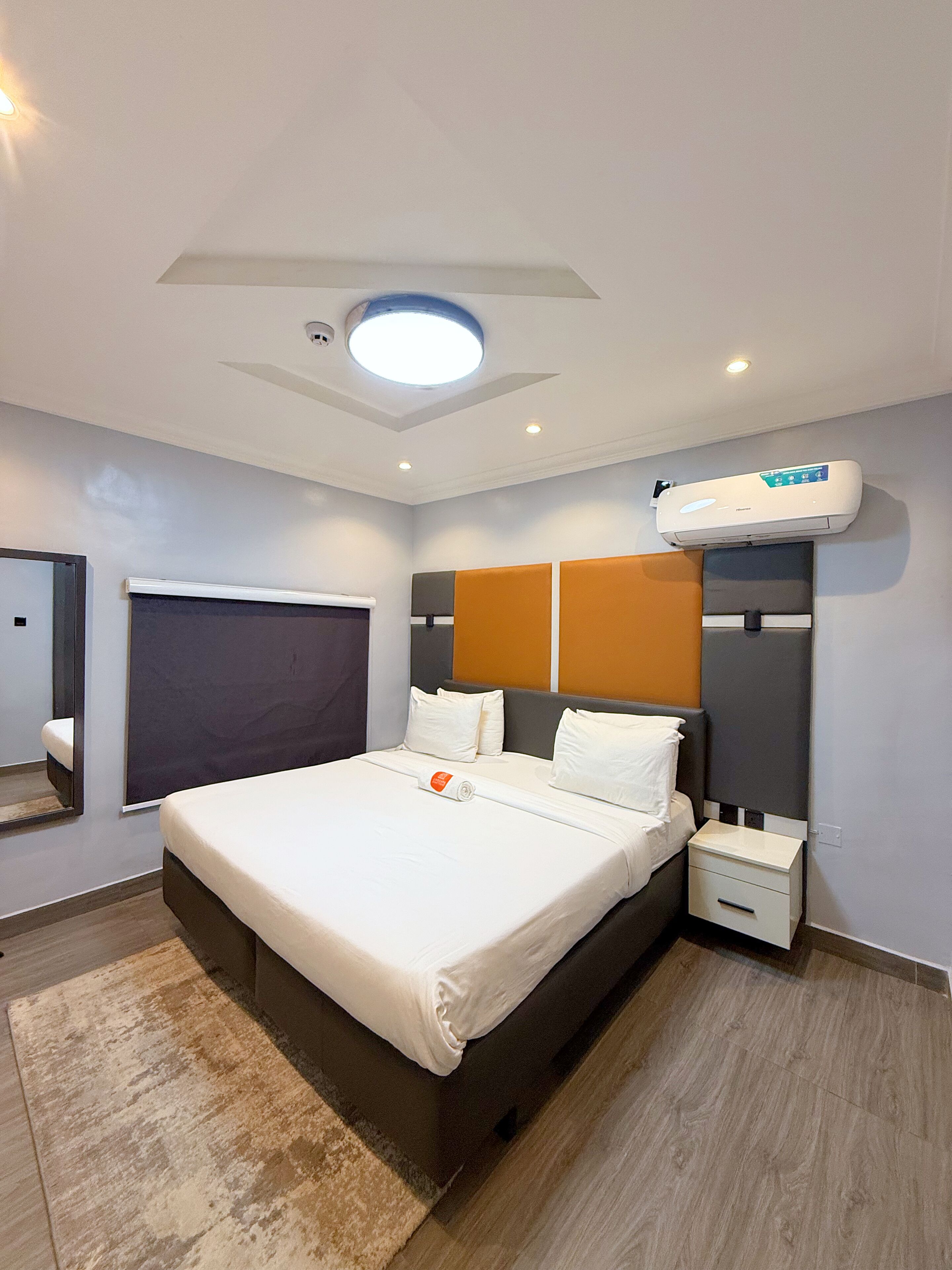 Ein modernes Hotelzimmer mit einem großen Bett, einem Nachttisch, einer Wand-Klimaanlage und einer Deckenleuchte.