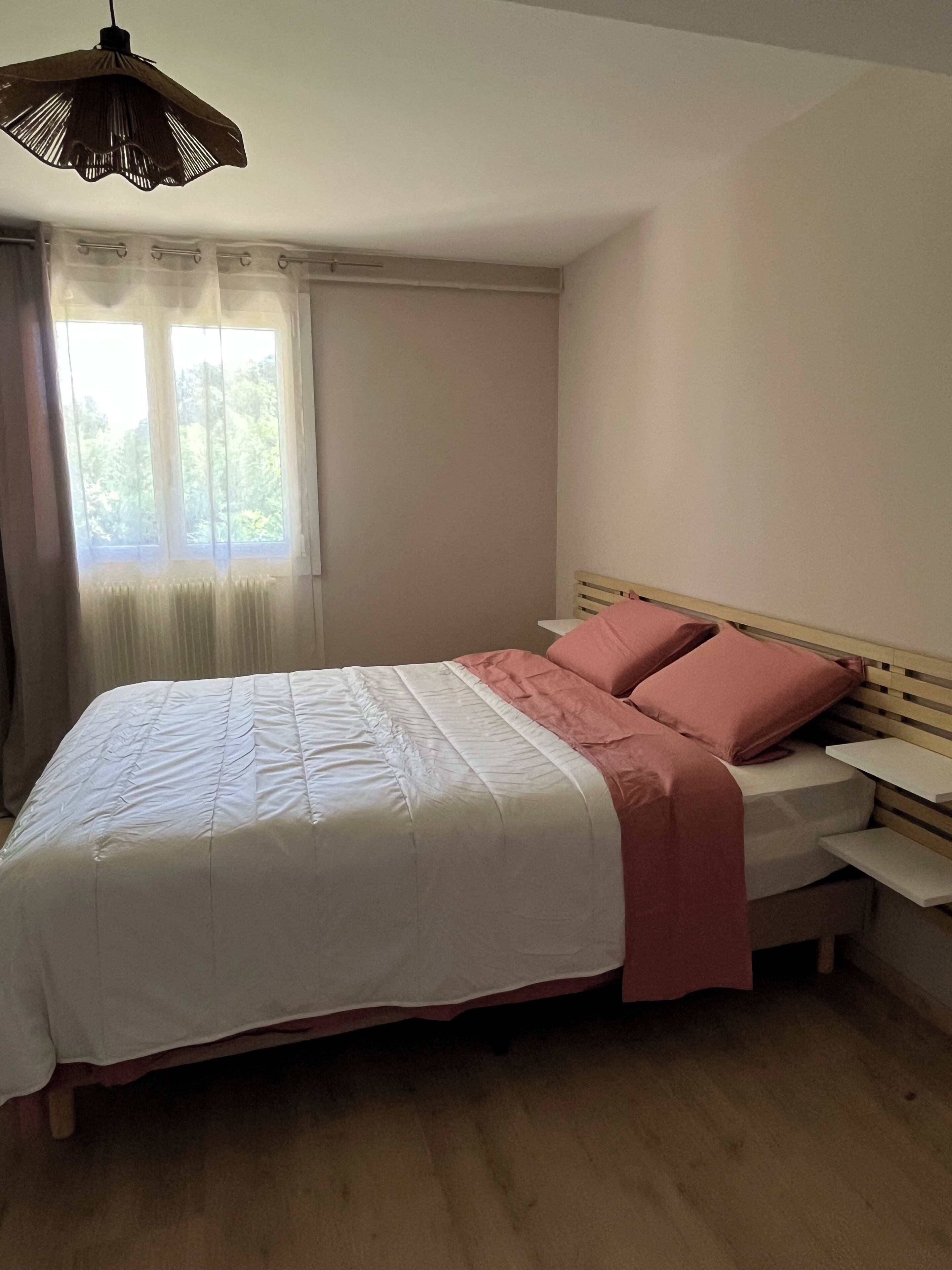 A bedroom with a bed, a window with curtains, a radiator, and a hanging light fixture.