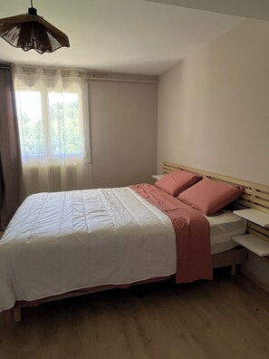 A bedroom with a bed, a window with curtains, a radiator, and a hanging light fixture.