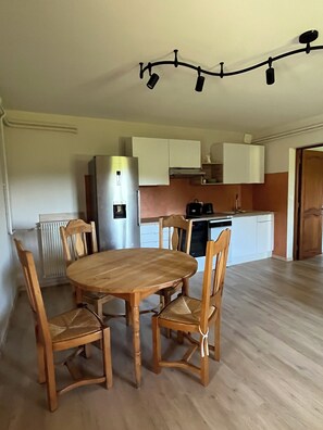 Een kleine keuken met een eettafel en stoelen, een koelkast en een koffiezetapparaat.