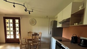 Een keuken met een eettafel en stoelen, een klok aan de muur en een koelkast.