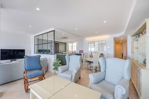 A spacious living area with a sofa, two patterned armchairs, a glass coffee table, a TV, and a kitchen in the background. - LXR Nice 3-Bedroom Oceanfront (Fuengirola)