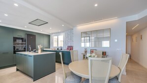 A modern kitchen with a central island, dining area with white wicker chairs, and a large mirror on the wall. - LXR Nice 3-Bedroom Oceanfront (Fuengirola)
