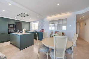A modern kitchen with a central island, dining area with white wicker chairs, and a large mirror on the wall. - LXR Nice 3-Bedroom Oceanfront (Fuengirola)
