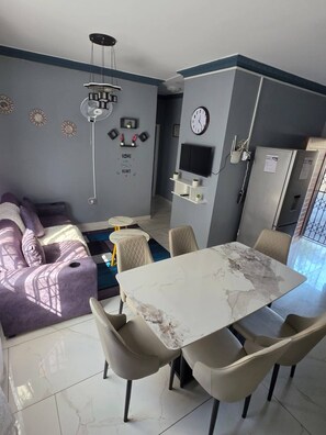 Een moderne keuken met een eettafel, stoelen, een bank, een televisie en een klok aan de muur.