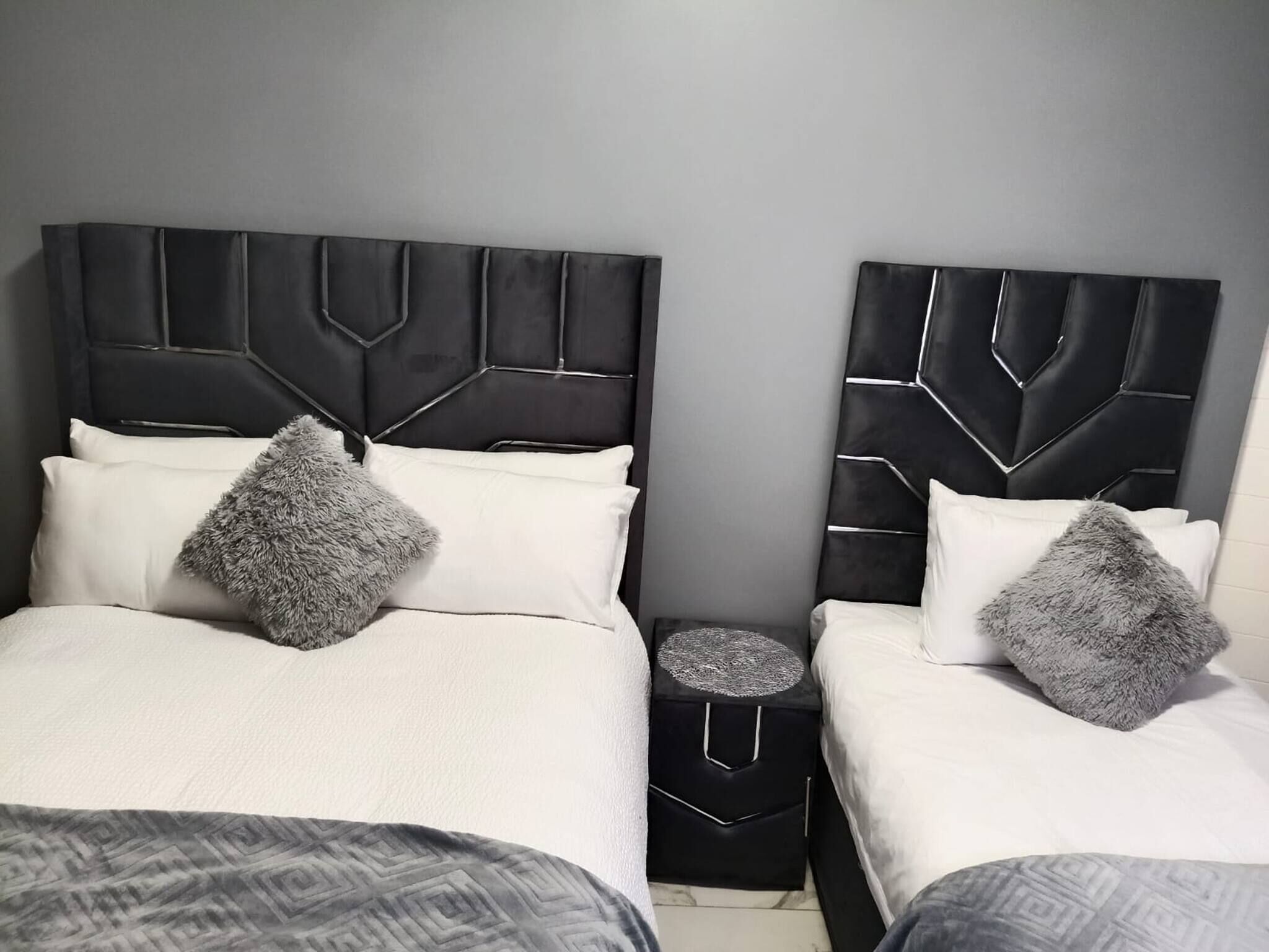 Un letto matrimoniale con testiera geometrica, un comodino e un cuscino decorativo grigio.