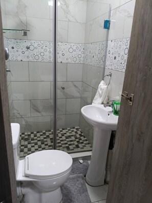 Un baño con inodoro, lavamanos, ducha con puerta de cristal y azulejos estampados.