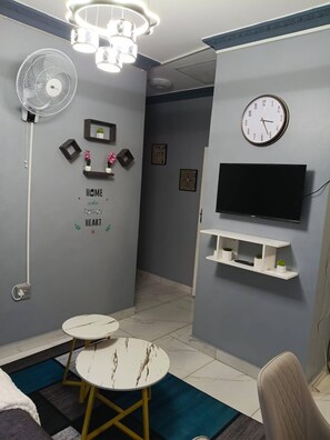 Una sala de estar moderna con un sofá blanco, una mesa redonda, un televisor sobre un estante blanco, un reloj y un ventilador.