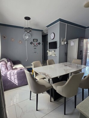 Een moderne woonkamer met een eethoek, een bank, een kroonluchter, een klok en een televisie.