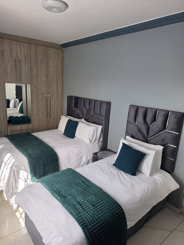 Habitación de hotel con dos camas, un panel de pared de madera, un espejo y piso de baldosas.